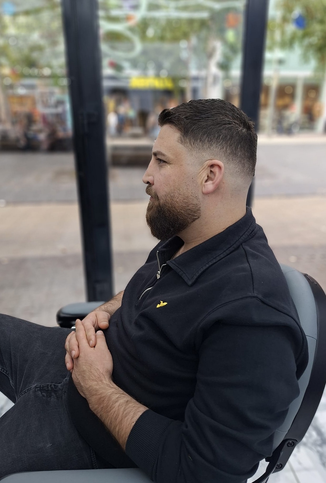 Klant in profiel met een fade en een bijgewerkte baard, bij het raam van de salon