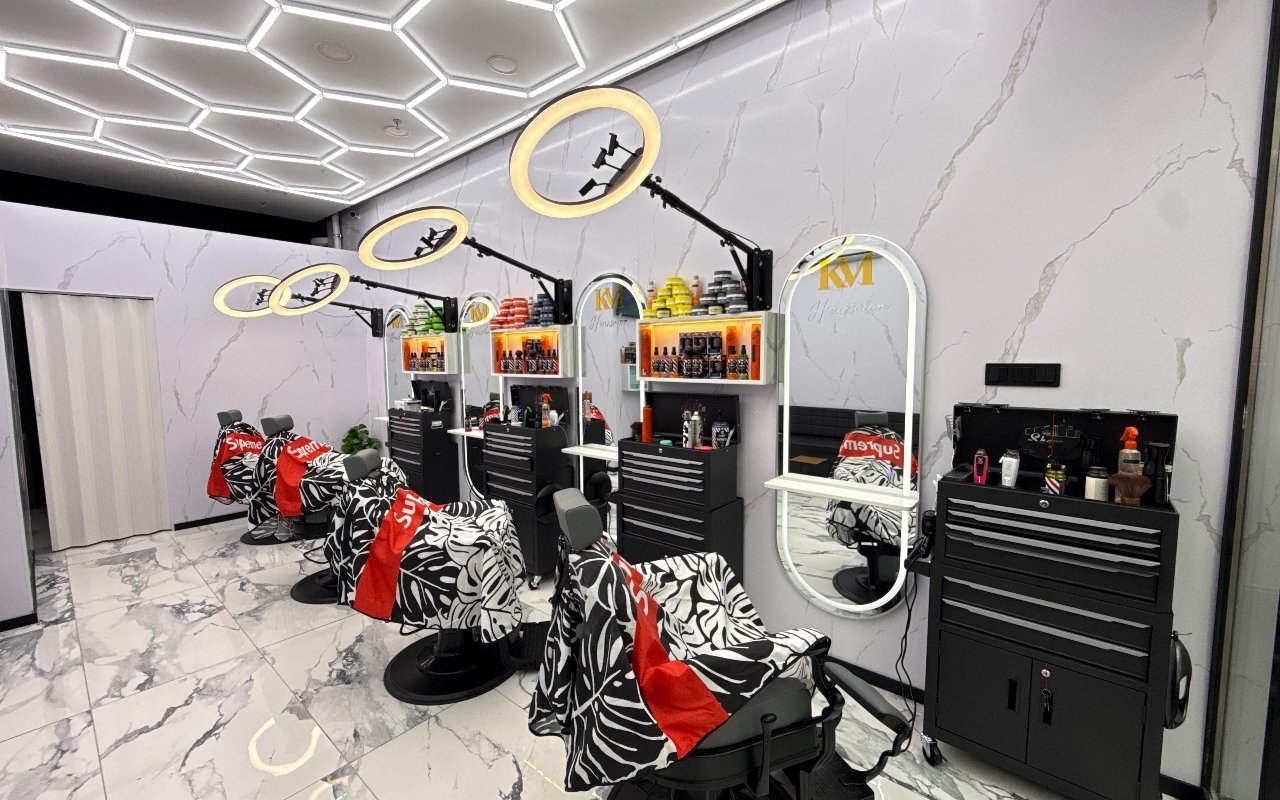 Interieur van KM Hair Salon: drie kappersstoelen met zebraprint capes, ringlampen, spiegels met het KM logo en het lichtplafond in zeshoeken