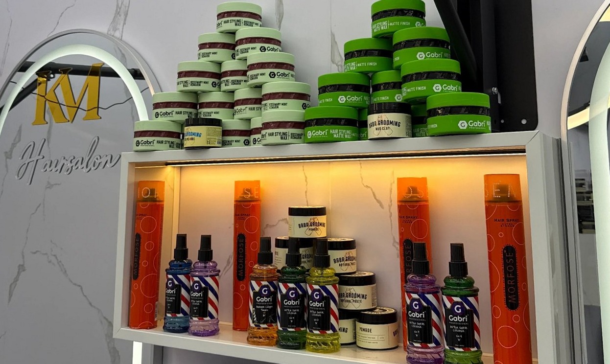 Verlichte schappen met stylingproducten naast een witte spiegel met het gouden KM Hairsalon logo